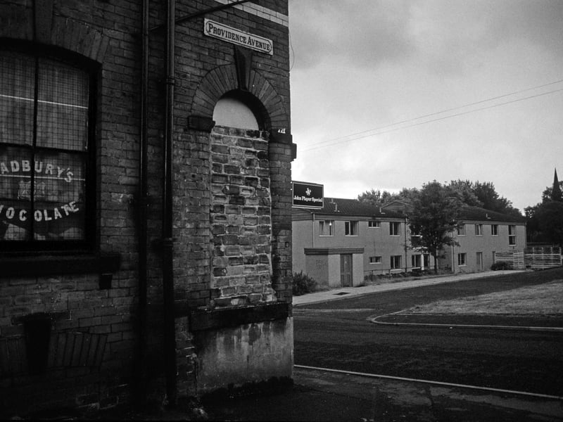 Providence Avenue at the junction with Delph Lane. A corner shop with a window bricked up has advertisements for Cadbury's chocolate and John Player cigarettes. Across Delph Lane is Delph View, where Delph Manor Adult Residential Centre can be seen. Pictured in August 1985.