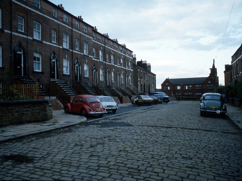 Looking east along Providence Avenue towards Quarry Mount Primary School on Pennington Street. Providence Avenue is a cobbled street with parking spaces on the left hand side and four-storey red brick terraced houses on both sides. Pictured in August 1985.