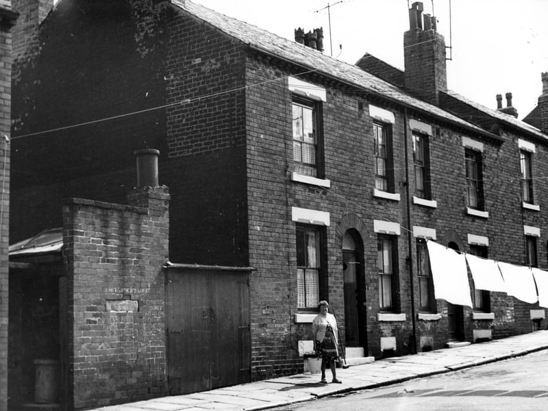 Servia Place in August 1967. To the left is a yard for dustbins and outside toilets. Number 7 has an open door, moving right is 9, then 11. A woman stands with her bucket and brush, water in the gutter suggests that she has been cleaning 'her' portion of the road.
