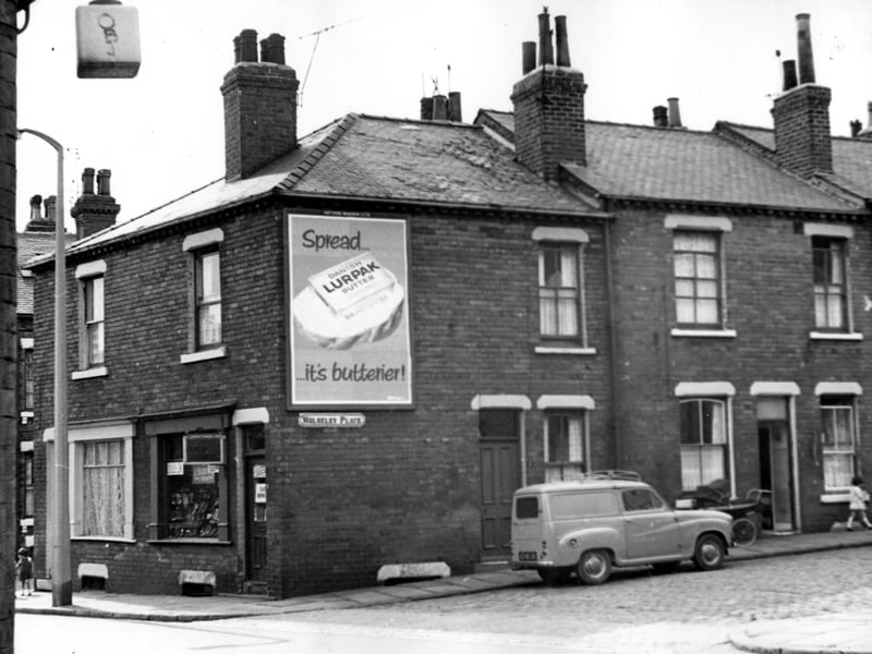 On the right edge is Wolseley Terrace then facing, on Cambridge Road numbers 5 and 7. A. Sigston and son have a shoe shop at number 7. Outside number 1 Wolseley Place an Austin van is parked. Number 3 is to right. A large poster is advertising Lurpak butter.