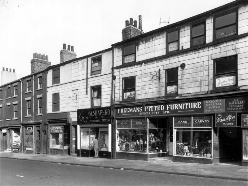 Shops and businesses on North Street. On the left edge is a shop and bakery, owner Mrs. F. Bloomfield. Moving right, next 172 has a notice in the window 'Wanted, Old Feather Beds'. Feather pillows are on sale for 4/- (20p) each. M. Shapero, optician is at 170. Phillip Freemans furniture shop is number 168. This shop went back onto Sheepscar Grove, where Freeman had a workshop.