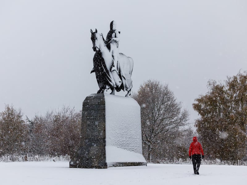 A man walks past the statue of King Robert the Bruce during heavy snowfall at Bannockburn, near Stirling.