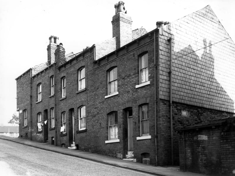 A row of three double fronted back-to-back terraced houses with Silver Royd Road on the left and a shared outside toilet yard on the right. Clothes hang on lines stretched across the house fronts of numbers 1 and 3 on the left.