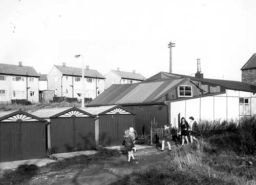 A group of school children in uniform walking past garages on the left and on the right the rear of number 375 Tong Road, the Joseph Tate funeral directors.
