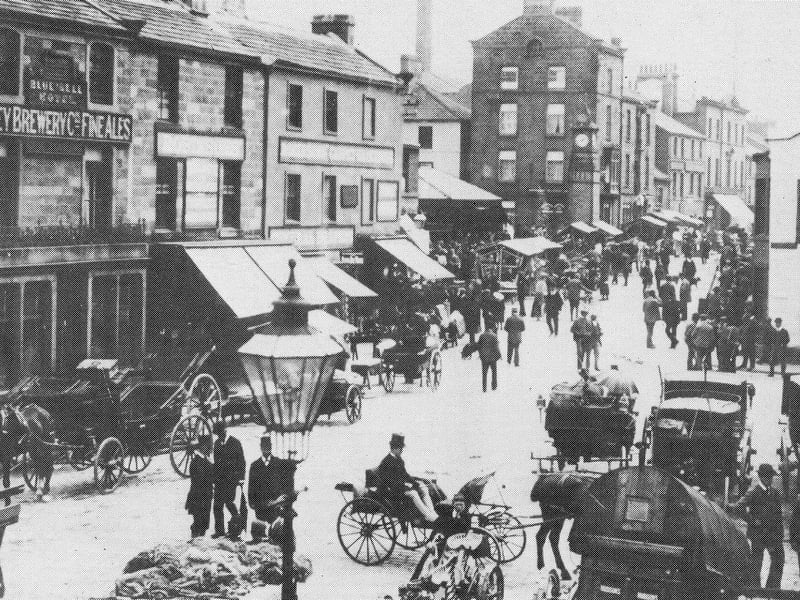 Looking from Manor Square towards Kirkgate on a busy market day, with many shoppers and horses and carts on the streets. On the left is Bluebell Hotel which closed in 1928.
