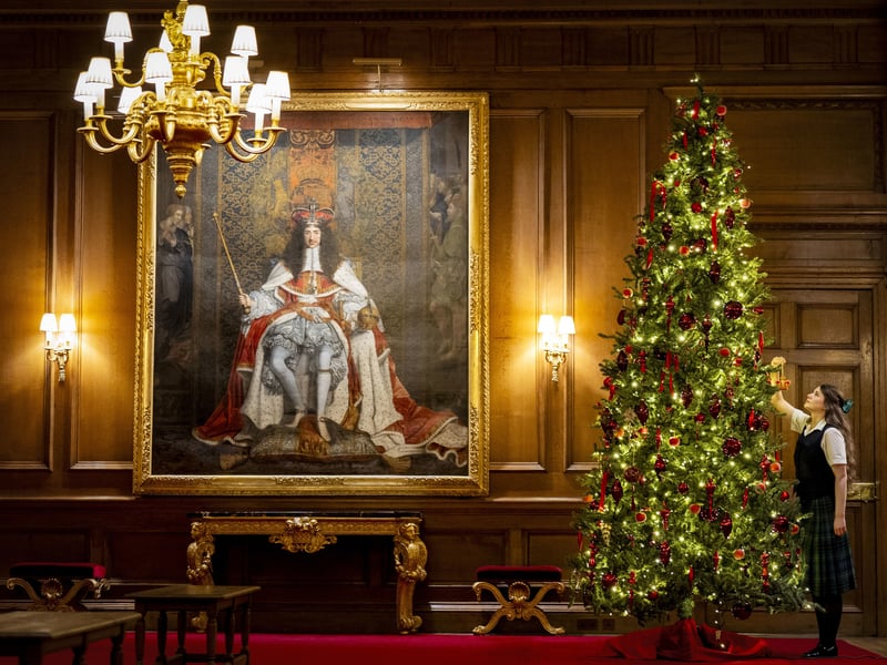 A member of staff putting the finishing touches to the Christmas Tree in the Throne Room at the Palace of Holyroodhouse in Edinburgh, where the exhibition will run. Picture: Jane Barlow/PA Wire