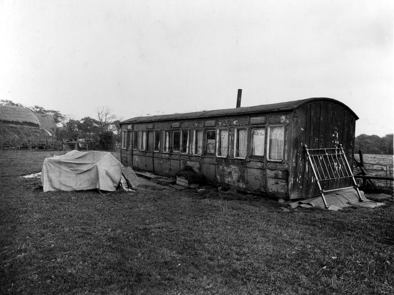 Barkers Farm, disused railway carriage, being used as a home. There are some hay stacks on the left. A brass bed end is propped against the carriage. Pictured in October 1936.