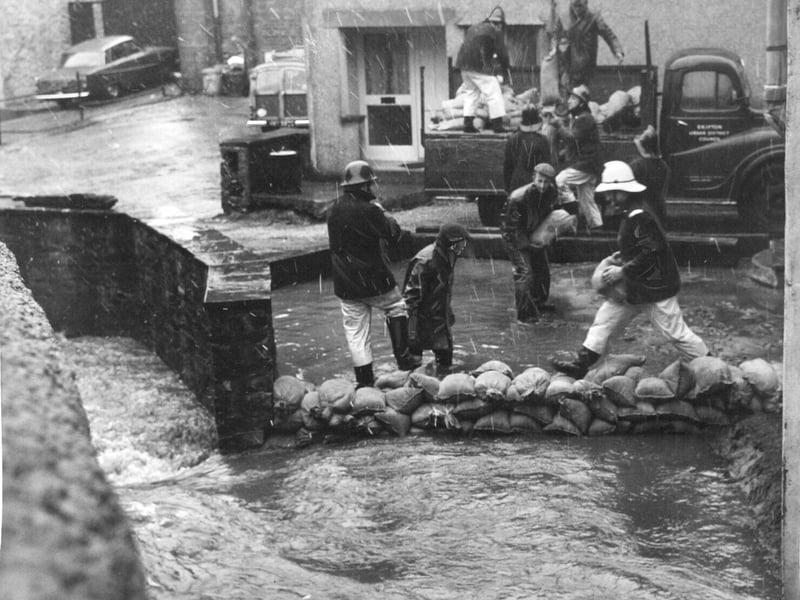Firemen and council workmen build a wall of sandbags as floodwater creeps towards shops and houses in March 1969.