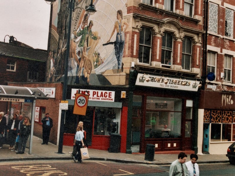Corn Exchange K6 bus stop to left, with Cornucopia a murla by Graeme Wilson painted on the side of Call Lane buildings. The parade of shops on Call Lane include; Jims Place, key cutting, Crown Fisheries and Milo, fashions. Pictured in September 1999.