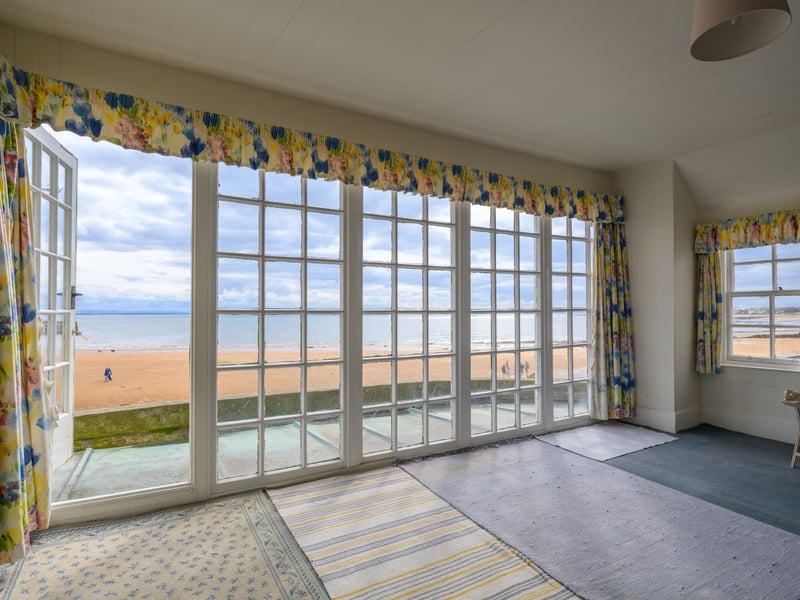 One of the four bedrooms has a wall of glass windows and a door out onto a balcony with a view of the beach