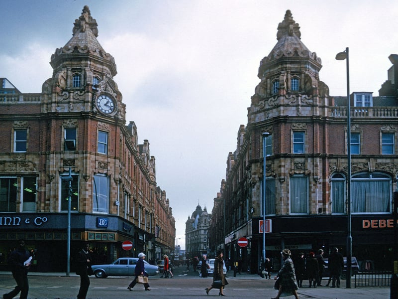Briggate showing the junction with King Edward Street in the centre. The two matching buildings on either side of the junction, with elaborate towers, are both Grade II listed buildings and were designed by Frank Matcham in 1898-1900 for the Leeds Estates Company as part of the County Arcade development. They are occupied here by Dunn & Co., menswear, and Debenhams department store. Kirkgate Market is seen in the background. Pictured in March 1975.