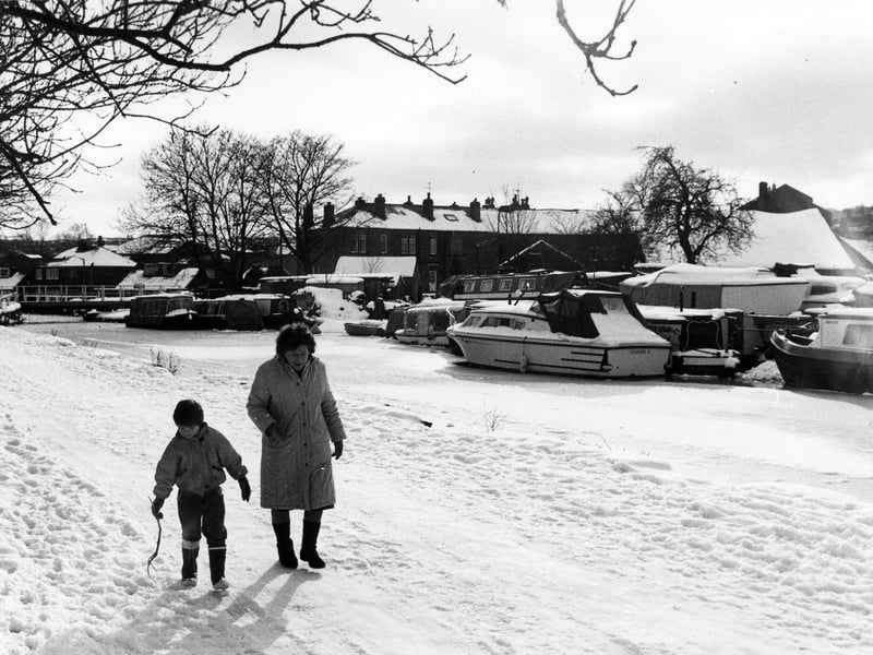 Barbara Sedgwick and her son Kevin are seen walking along a snow-covered towpath beside the Leeds and Liverpool Canal. Several barges can be seen on the canal, which appears to be covered with ice.