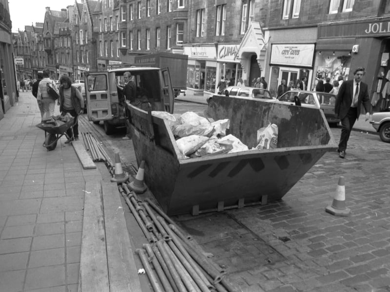 Workmen with a wheelbarrow and a skip full of builders rubbish as construction continues in Cockburn Street Edinburgh, August 1985.
