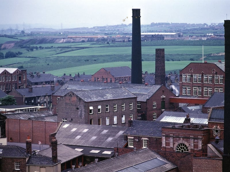 A view from the Town Hall tower towards the mill buildings in central Morley. The telephoto lens makes the buildings appear bunched together. On the left hand side, with the white roof, is the back of Park Mills which faces on to South Street. The buildings in the centre with two chimneys together are part of Peel Mills.