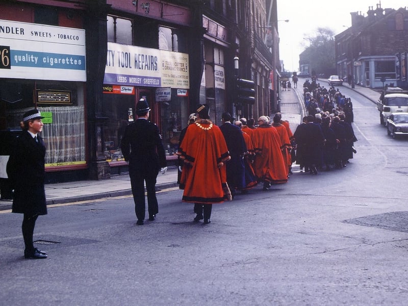 The procession for the last Annual Mayor's Sunday Service Parade of Morley Borough Council seen going up Chapel Hill from Morley Bottoms, on their way to St. Peter's Church from the Town Hall. Policewoman stands guard in the centre of the road as aldermen in their red robes are among those who have just passed. Shops on Cheapside are seen on the left of the photo from May 1973.