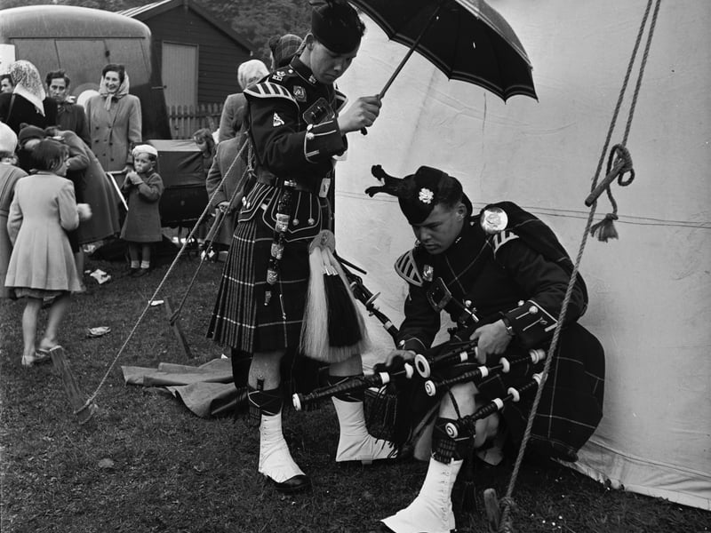 A Scottish piper takes cover under a colleague's umbrella whilst he adjusts his pipe during a ceremony on the Isle of Skye in 1955.