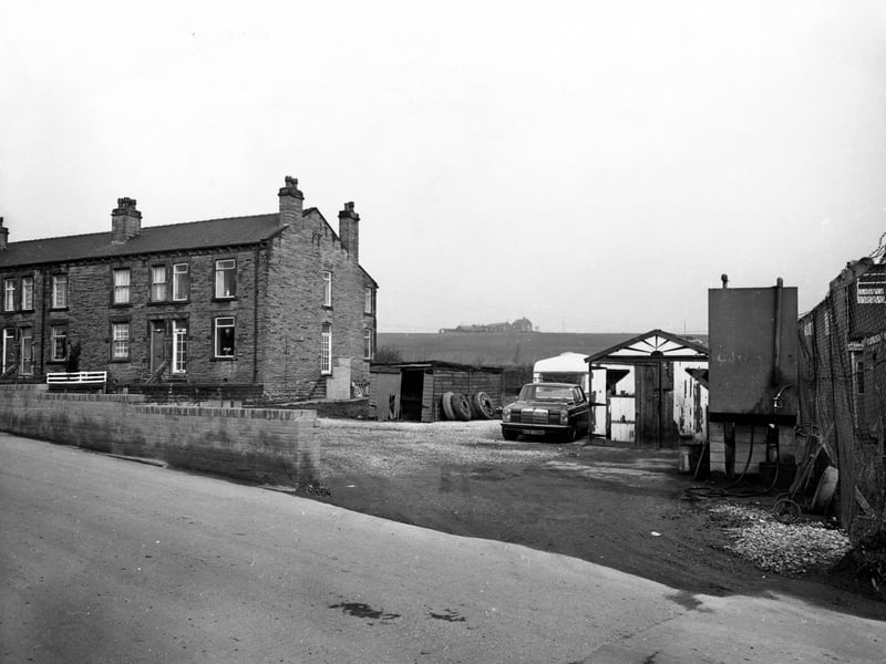 View shows part of Woodview Terrace, a short terrace of houses on Quarry Lane, Woodkirk. On the right is a yard with a car, a caravan, a garage and a shed with tyres piled up against it. Pictured in October 1980.