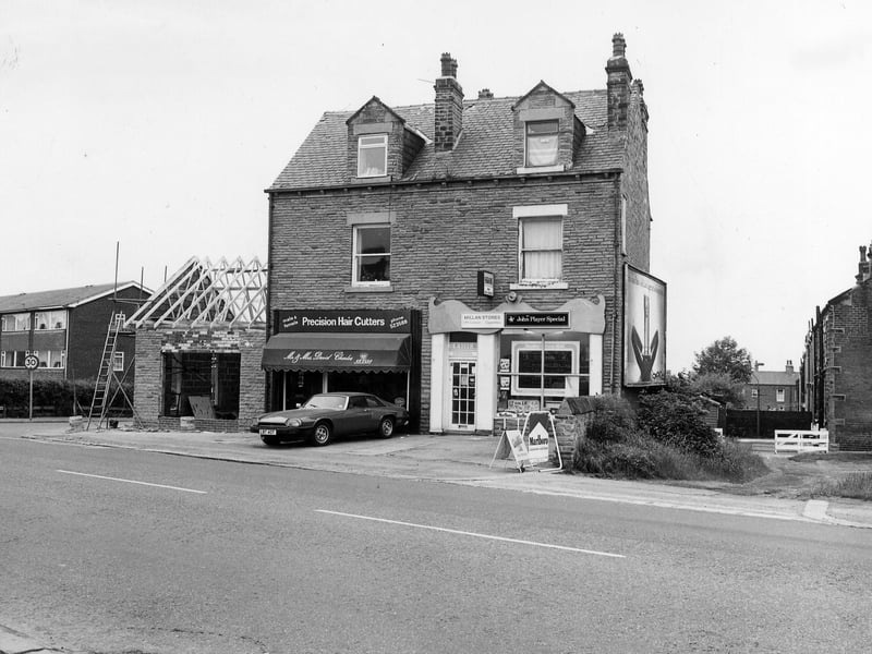 The south side of Bradford Road showing a pair of shops in the centre; to the left is Mr. & Mrs. David Charles, precision hair cutters, at no. 29 and to the right Millan Stores, off licence and cigarettes, at no. 31. To the left of no. 29 a single storey extension is in the process of being built. Next to this is the junction with Beech Street then further left a block of houses numbered 21 to 27. On the right is the edge of a row of houses which faces onto Fenton Street, just off the photo from June 1983.