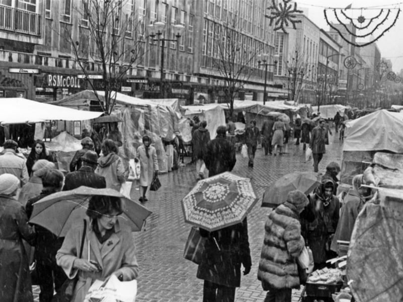 Shoppers at the outdoor market on The Moor, Sheffield city centre, on a rainy day in 1980, with shops including Etam and RS McColl in the background