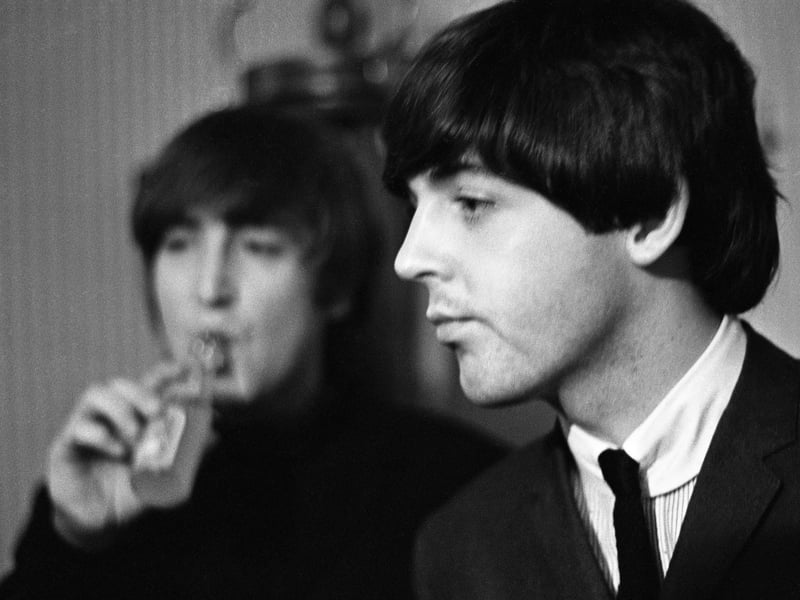John Lennon drinks a refreshing lemonade as Paul McCartney looks on in their dressing room at the Odeon Theatre in Leeds on 22 October 1964.