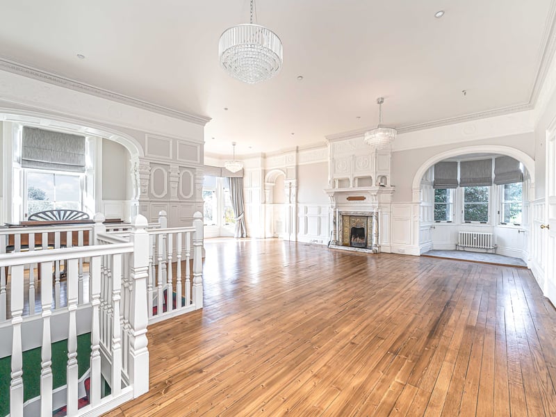 An expansive lounge rich with period features, including an ornate fireplace and large windows that frame views of the castle’s well-groomed gardens