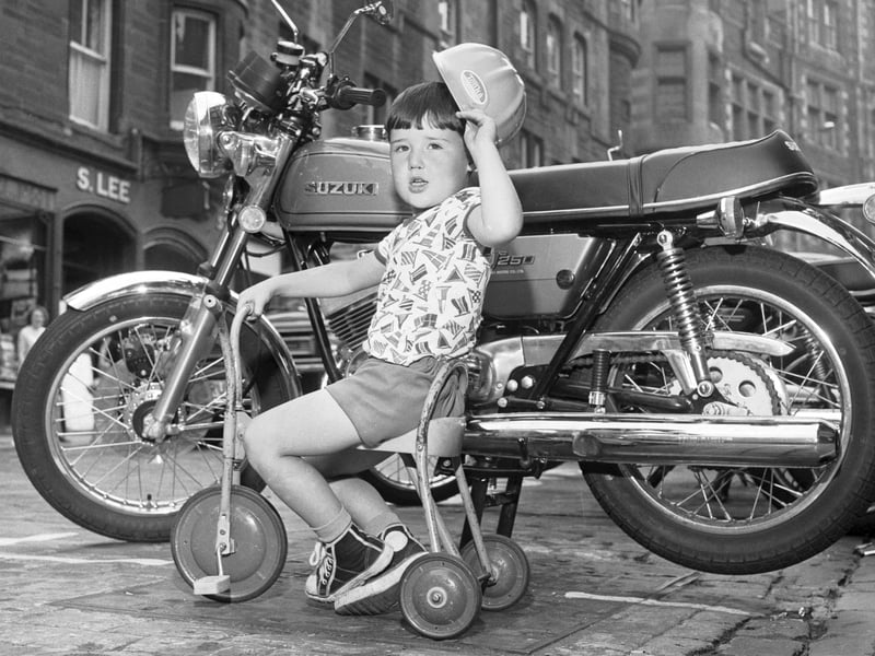 A little boy on his tricycle in Cockburn Street wants to ride a Suzuki motorbike when he grows up, July 1976.