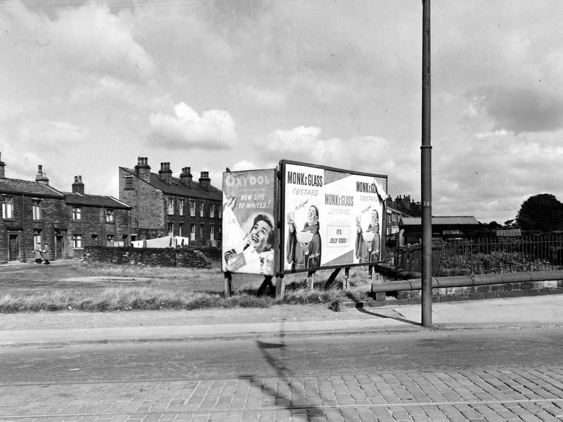 An advertising hoarding on the site of number 186 Stanningley Road. Posters for Oxydol clothes whitener and monk and glass custard. To left is a row of terraced houses outside of which stand two men holding newspapers. Pictured in September 1951.