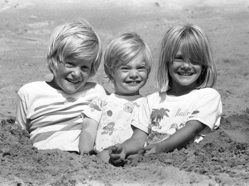 Three girls half-buried in the sand on Portobello beach as the sun shines in July 1989