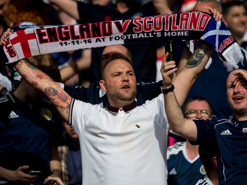A Scotland fans raises his matchday scarf above his head.