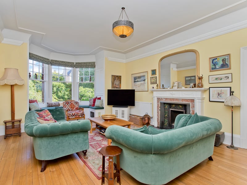 The impressive living room occupies a generous footprint, offering excellent flexibility for endless configurations of furniture, with a beautiful fireplace creating an ideal focal point around which furniture can be arranged. The room is fronted by a large bay window with a charming window seat where leafy garden views can be enjoyed, and it is decorated in pared-back tones, enhanced by a picture rail and warm wood flooring.