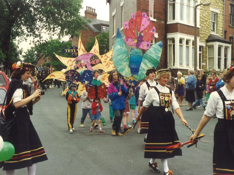 Kirkstall Festival in July 1991. The parade makes its way along Hesketh Road. Children are carrying home made models and Briggate Morris dancers can be seen with smocks, clogs and decorated bobbins.
