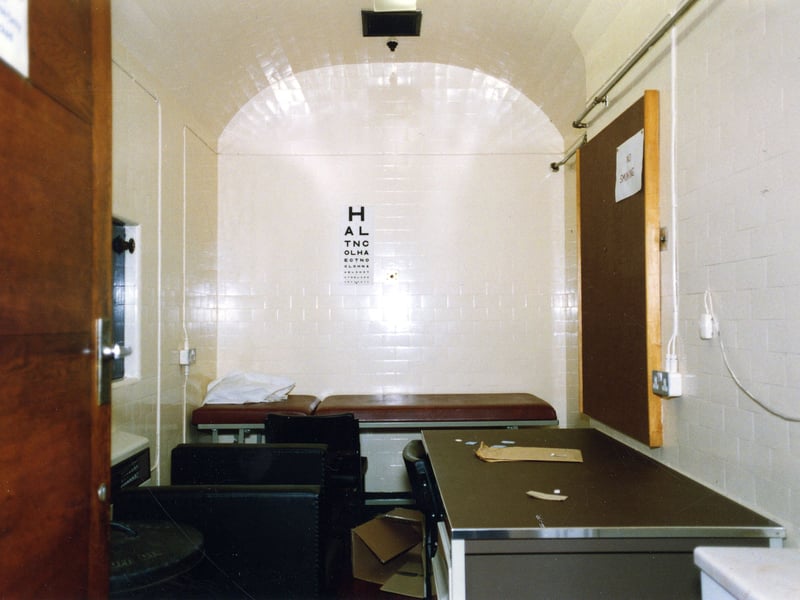 The Doctor's Room. The room is simply furnished with a desk and chair and a bed for the examination of prisoners who are injured or ill. There is a sight chart on the wall for eye examinations.