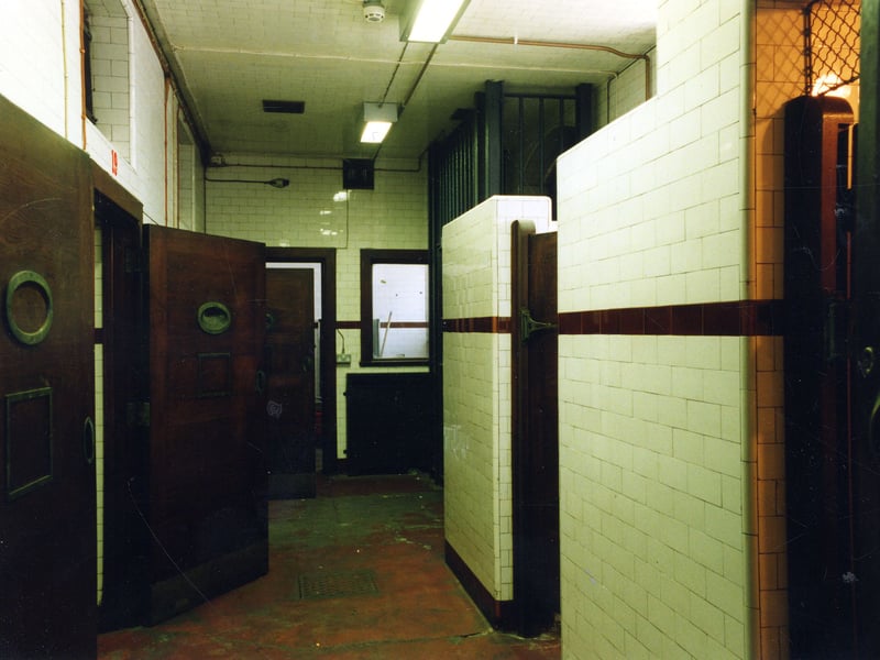 The van gate Assembly The metal gateway gives access to Oxford Place. On the left an open door to cell 19 is visible. Cells 18, 19 and 20 were converted during the improvements of 1864 from the original living accommodation of the gaoler and his wife. They are sometimes known as 'the gates' or 'the cooler'. Central heating panels are cemented into the rear walls. Toilet facilities are visible on the right and at the far end is the prison staff room.