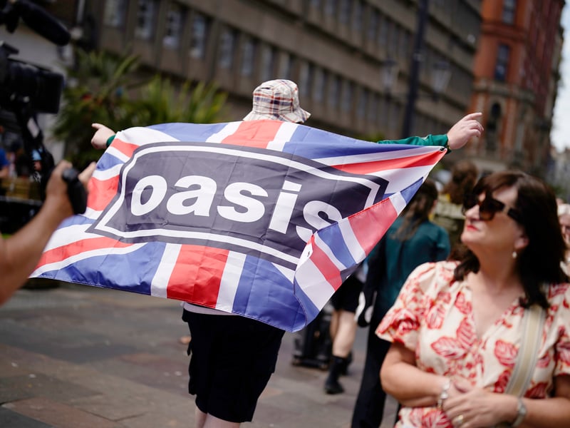 An Oasis fan holds a Union Jack flag featuring the band logo in Cardiff.