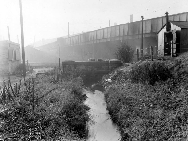 A view of Balm Beck as it flows towards low stone bridge. Railway track is visible behind. In the background is a larger bridge carrying Balm Road across the railway. Pictured in November 1949.