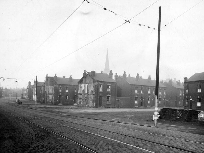 Looking north across Balm Road to Barmouth Road and Terrace in November 1943. Four rows of back-to-back houses are to the centre, each having the end house demolished, revealing the interior walls, floors, fireplaces and chimney flues.o the right, a low wall behind which can be seen part of Barmouth Place. Behind the left hand pole is a fire hydrant painted white for war use. The houses on Barmouth Road have entrances to the outside toilets between them.