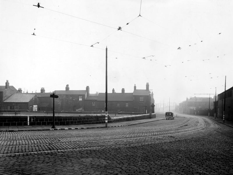 A view of Balm Road looking south onto Tate Place in November 1943. The cobbled road has tram lines and is bordered by poles supporting the overhead power cables for the trams.Beyond the road, a low stone wall leads to large stone gate posts allowing entry to the graveyard of St Mary's Church with wooden benches.