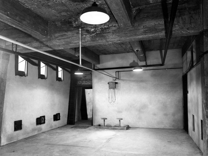 Inside the Public Bath House South Brook Street in October 1942. It is difficult to tell from the view of this internal room at the bath house exactly what its function was. There are two stools in a sunken bath type enclosure above which is a tap filled cystern with two rubber hoses. A rail runs the length of the room and it holds what appear to be curtain rings.