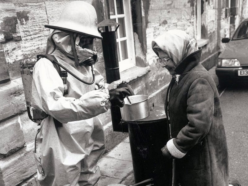 Firefighter Dan Richards, wearing full nuclear fallout gear, cooks a meal in the war bunker site at Cusworth Gala, Doncaster, watched by Elsie Nayler, in January 1988