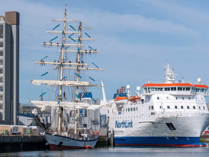 A full image of the Fryderyk Chopin, the youngest of the polish ships, beside a ferry in the harbour. It has a total length of 54.74 metres, and a long bowsprit which means she can set five headsails and take advantage of light winds