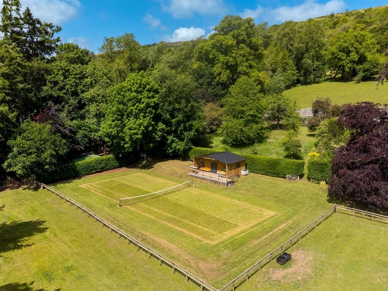 A full-size grass tennis court is positioned at the bottom of the garden.