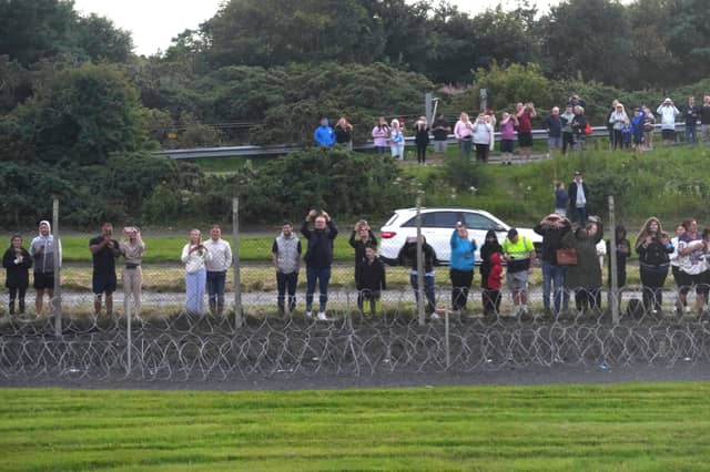 Onlookers stand at the fence near the runway
