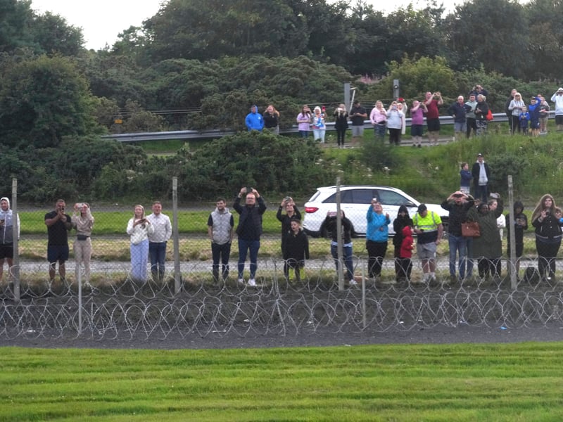 Onlookers stand at the fence near the runway