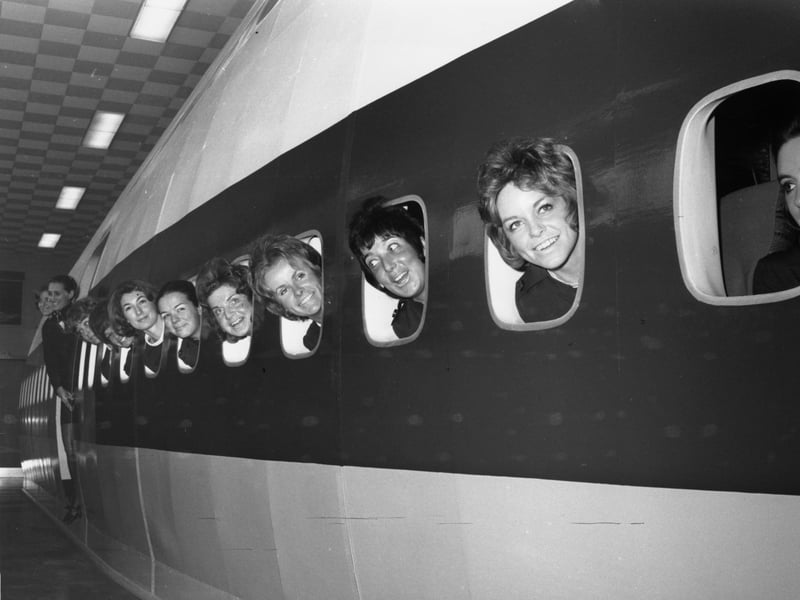 BOAC trainee stewardesses looking out of the portholes of a mock-up plane in March 1971