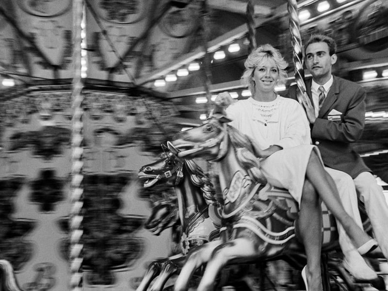 A young holidaymaker rides the merry-go-round with a Redcoat at the Butlin's Holiday Camp in Bognor Regis, West Sussex, in June 1985