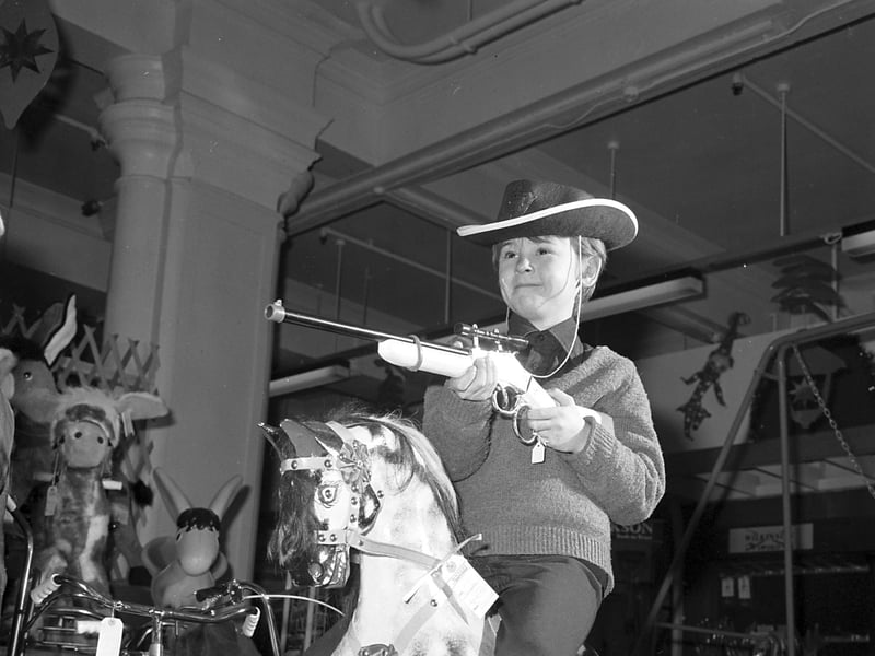 A little boy with a cowboy hat and a toy rifle on a rocking horse in the toy section of Jenners department store, Edinburgh, in December 1977