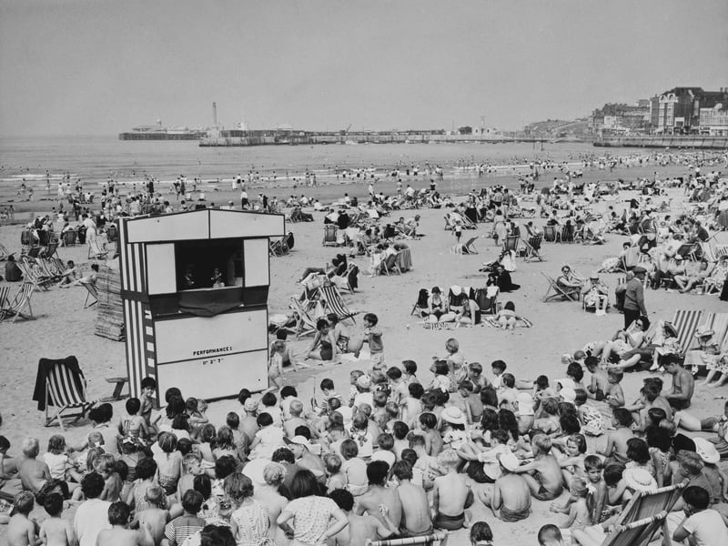 Holidaymakers watch a Punch and Judy show on the beach, with Margate Pier extending in the distance, in July 1961