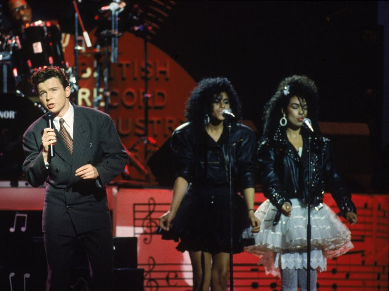 Rick Astley performs with two backing singers at the BPI Awards in 1986