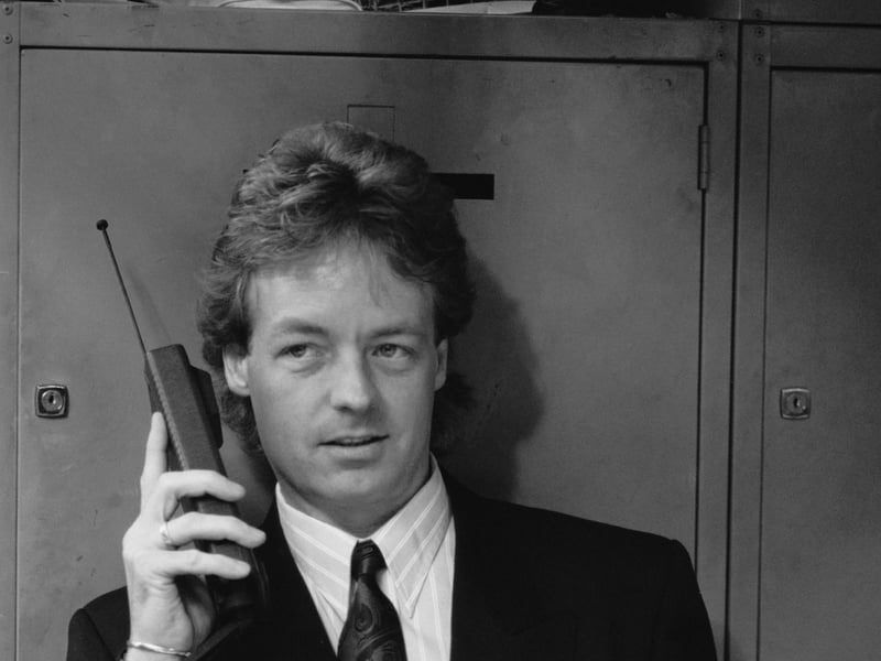 A besuited man using an early mobile phone and holding a Filofax personal organizer, two of the must-have accessories for any eighties businessman, in October 1988