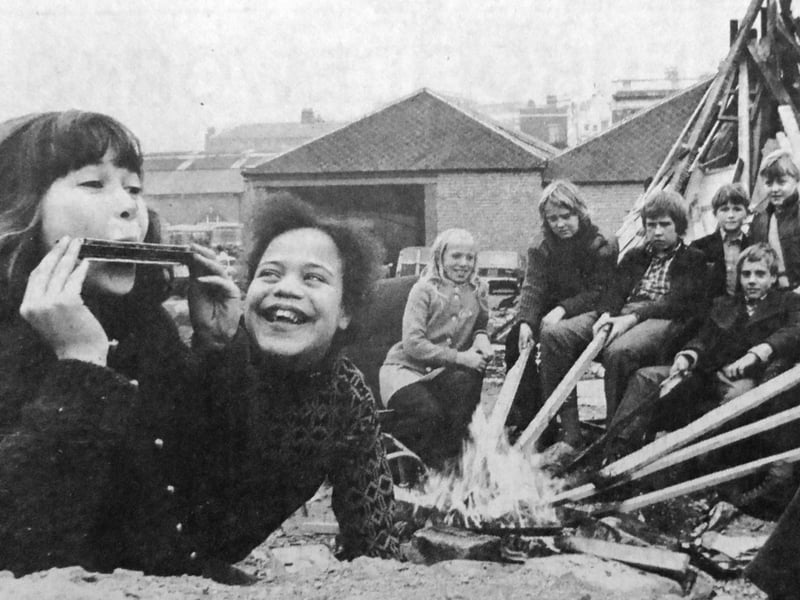 Children sit near their bonfire at Hyde Park Road, Southsea, roasting potatoes on a small fire, with Sally Farley, 10, on the mouth organ